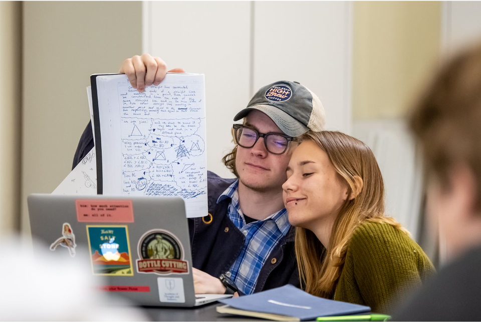 Guidepost Academy students sitting at a laptop holding up a notepad